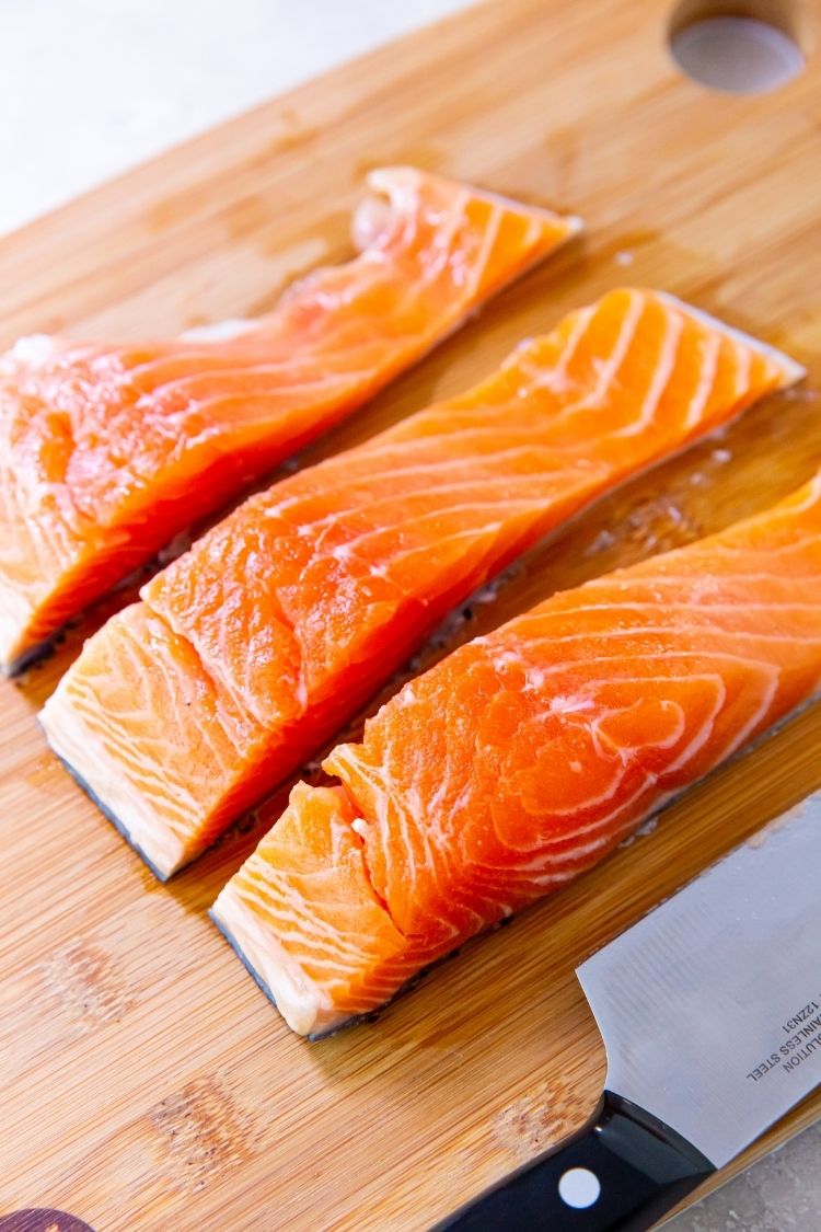 3 salmon filets on a wood cutting board with a knife