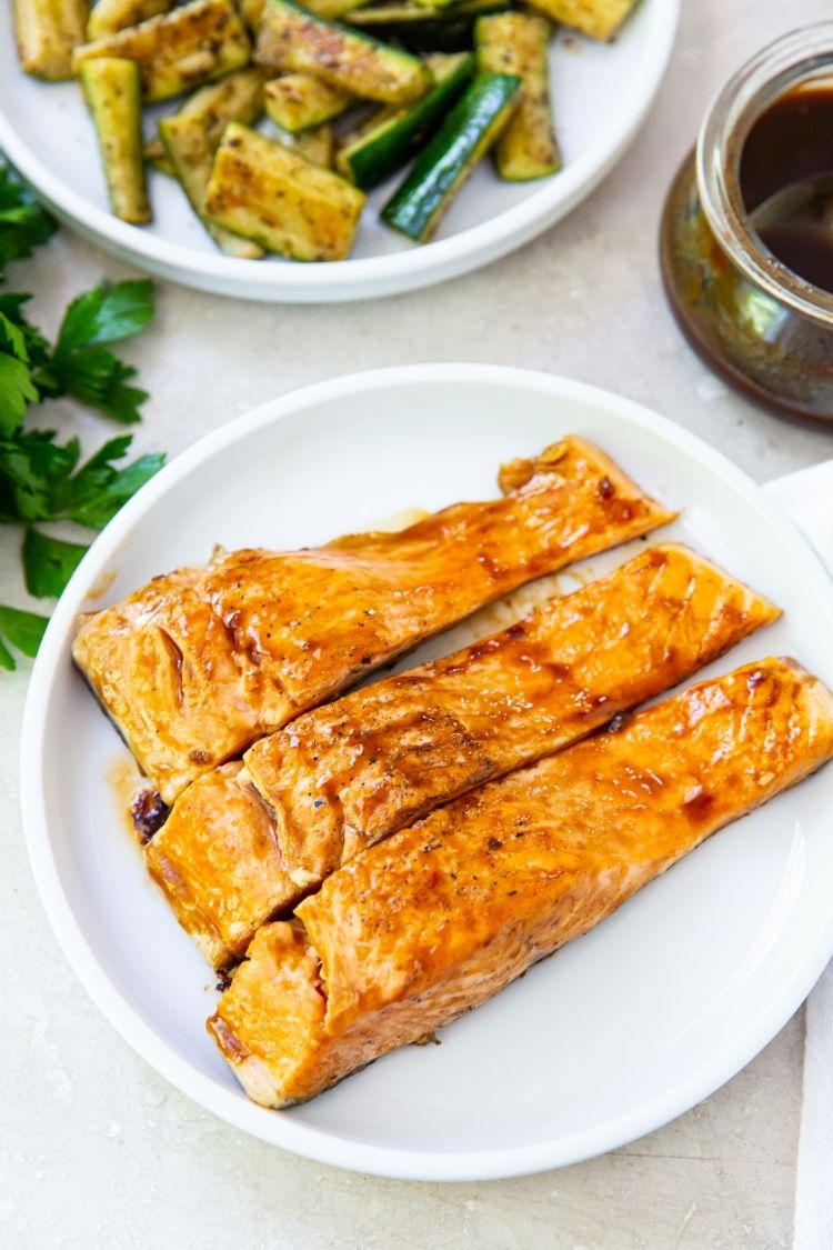 grilled teriyaki salmon filets on a white plate with parsley on the table