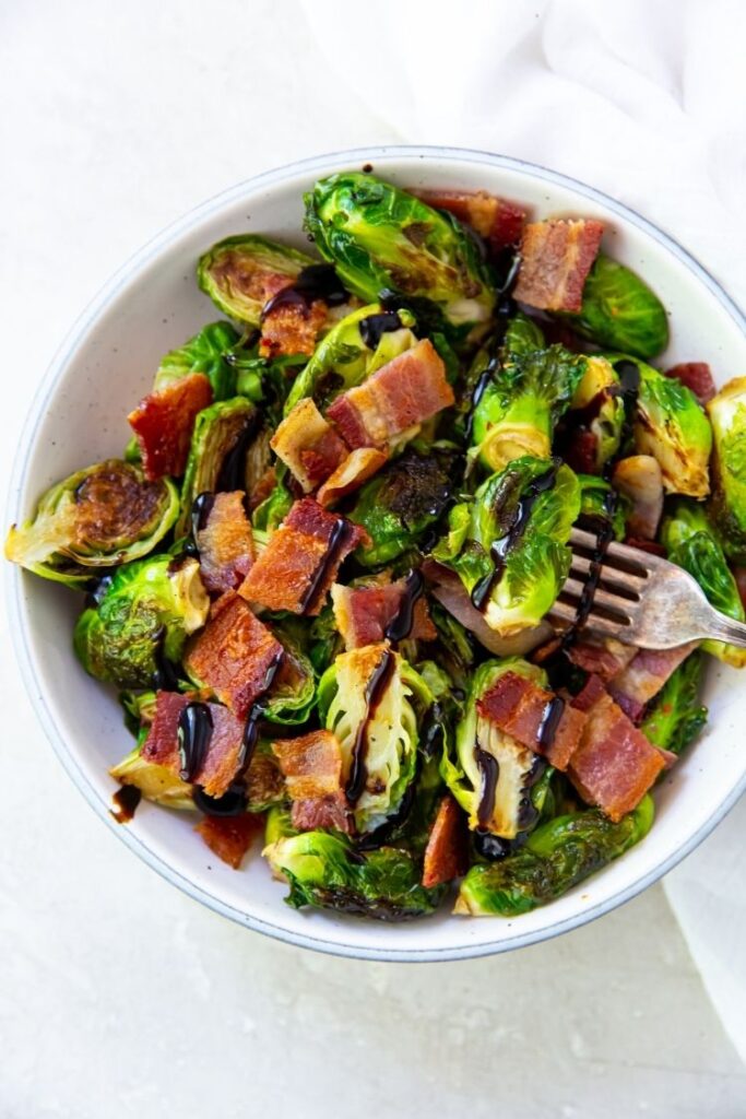 Brussel sprouts with bacon topped with balsamic glaze in a white bowl with a fork