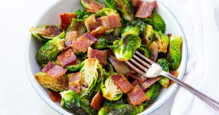 Brussel sprouts with bacon in a white bowl with a fork