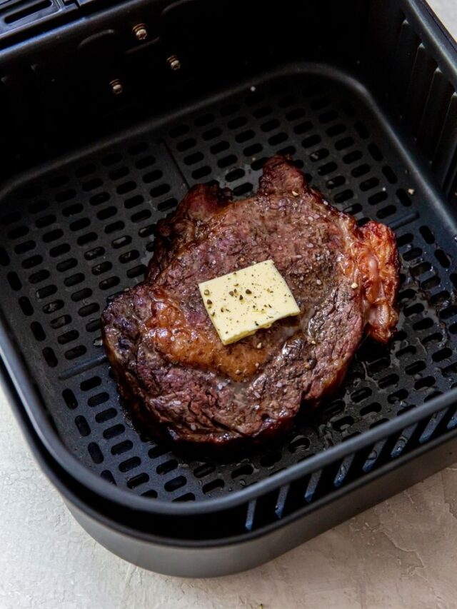 a cooked ribeye steak in an air fryer basket topped with butter and spices
