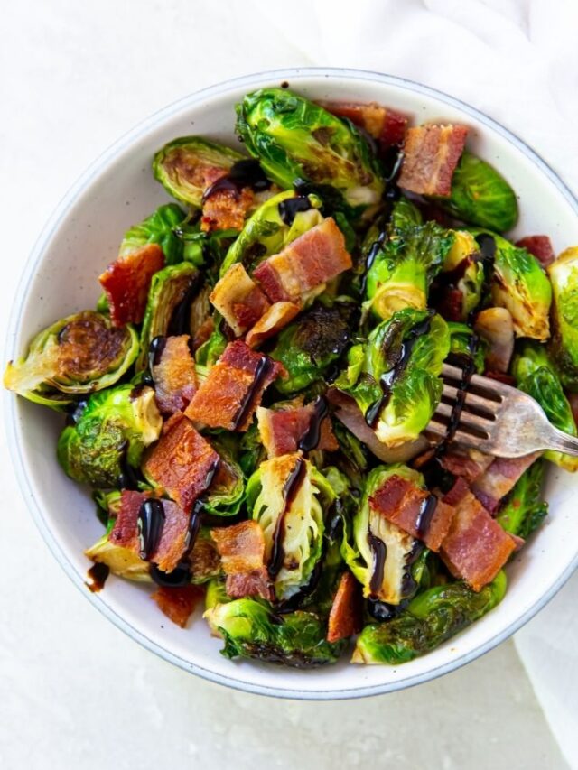 Brussel sprouts with bacon topped with balsamic glaze in a white bowl with a fork