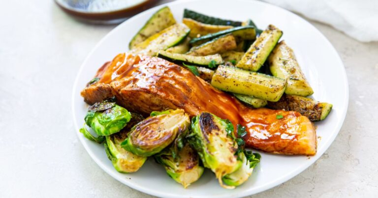 Salmon on the Blackstone Griddle with brussel sprouts and zucchini on a white plate.