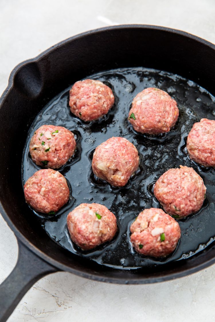 raw keto meatballs being cooked in a cast iron skillet