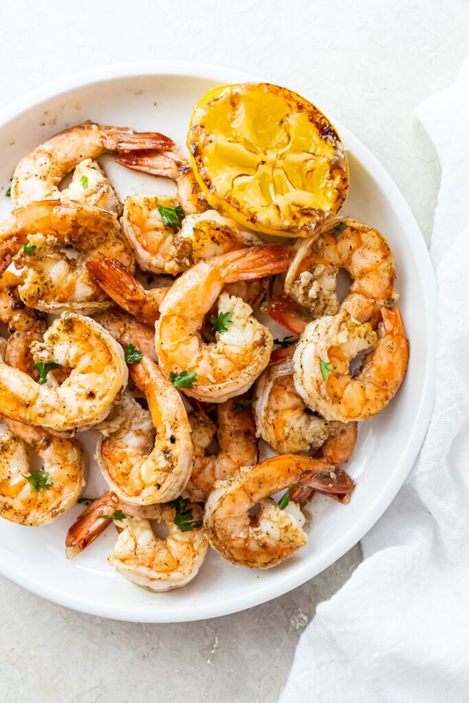 Griddled shrimp topped with parsley, garlic and lemon juice on a white plate