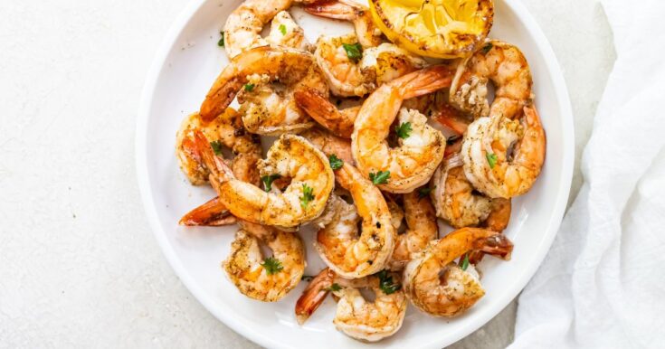 Grilled shrimp topped with parsley, garlic and lemon juice on a white plate