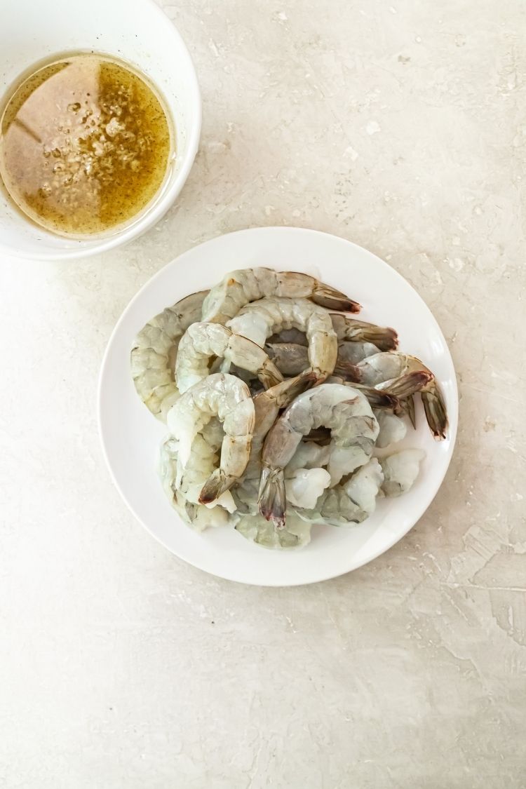 raw shrimp on a white plate with a bowl of oil