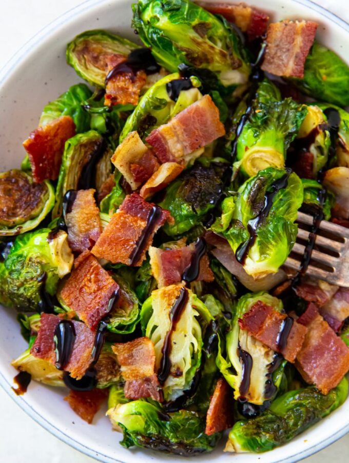 Brussel sprouts with bacon in a white bowl with a fork