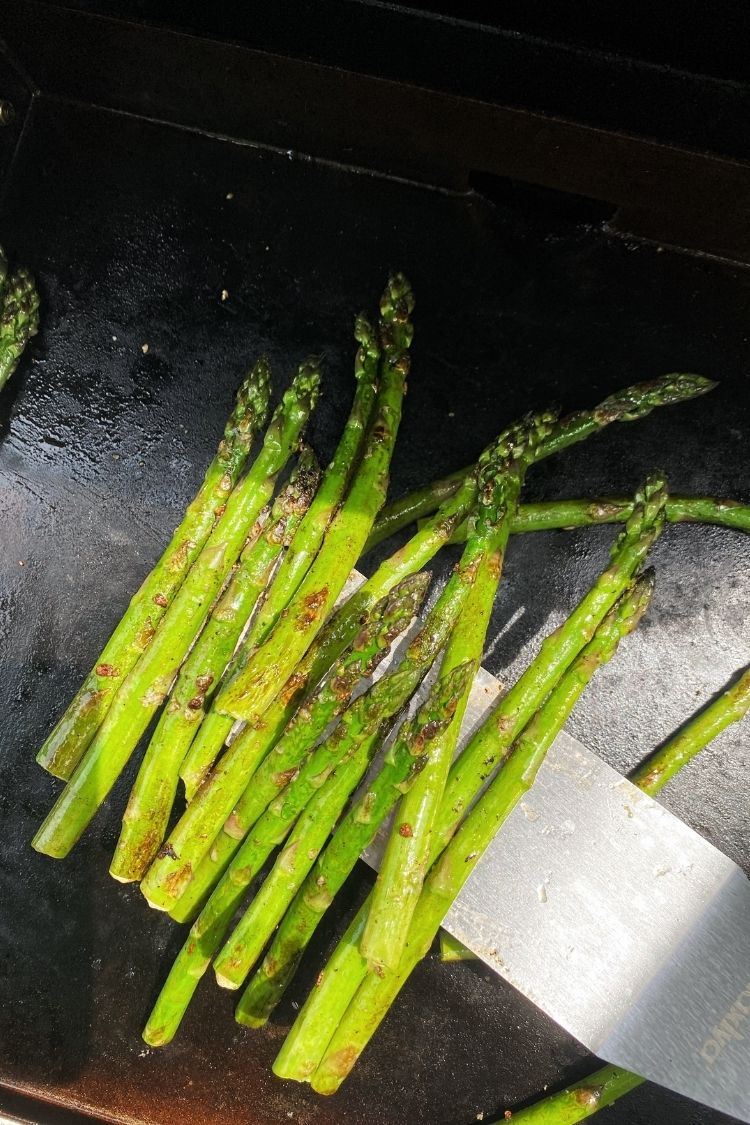 cooked asparagus on a blackstone grill and spatula