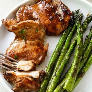 sliced teriyaki blackstone chicken thighs on a white plate with griddled asparagus