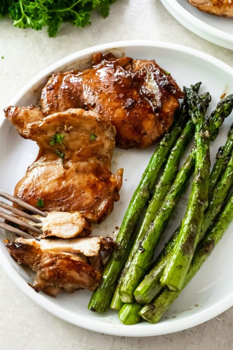 sliced teriyaki blackstone chicken thighs on a white plate with griddled asparagus