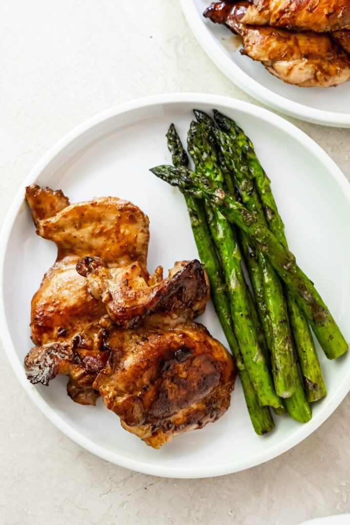 teriyaki blackstone chicken thighs on a white plate with griddled asparagus