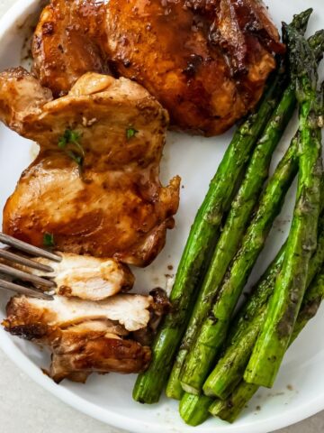 sliced teriyaki blackstone chicken thighs on a white plate with griddled asparagus