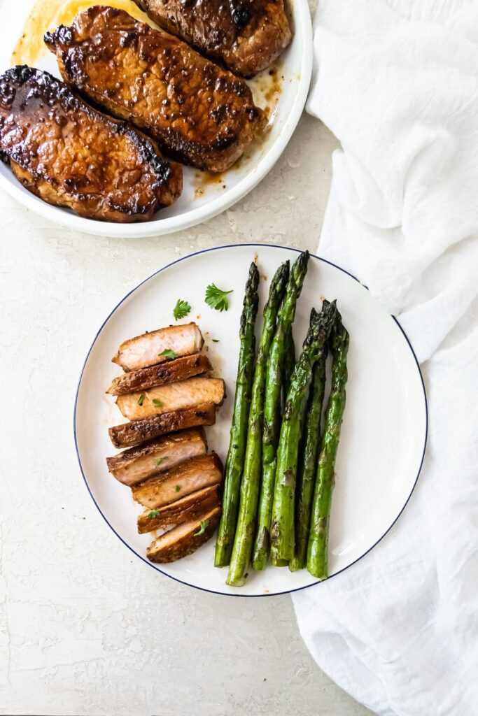 cut up grilled pork chops on a white plate with asparagus