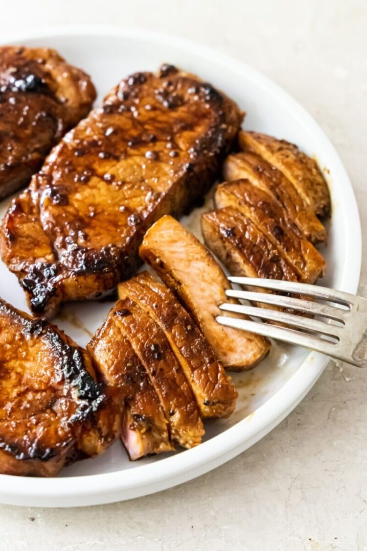 Grilled pork chops on a white plate with a fork