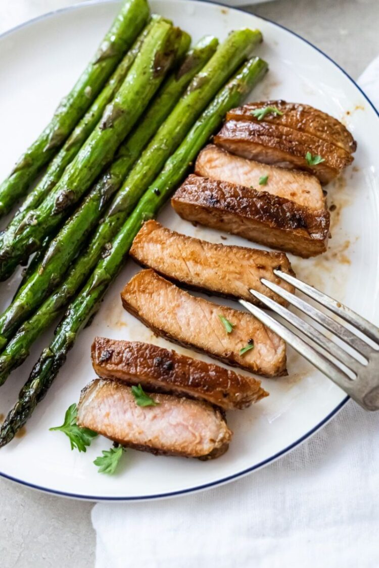 cut up grilled pork shop on a white plate with asparagus