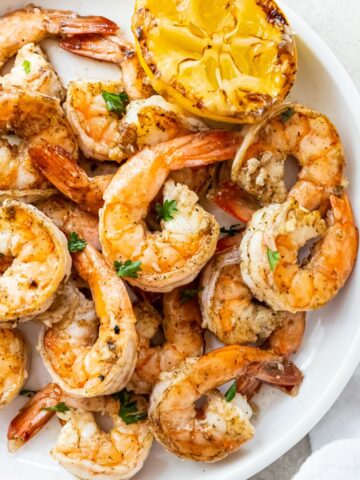 grilled shrimp topped with parsley on a white plate with a lemon half