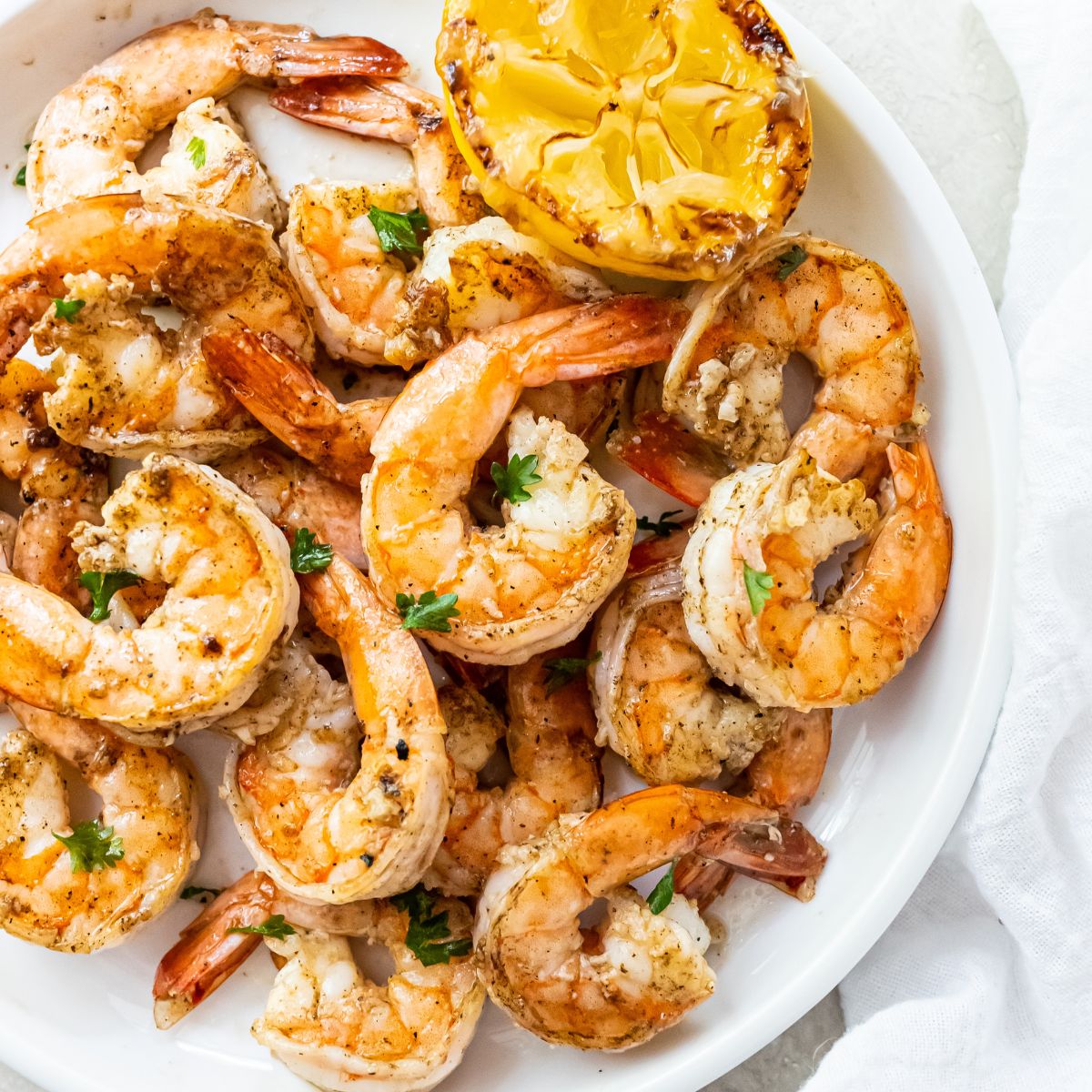 grilled shrimp topped with parsley on a white plate with a lemon half