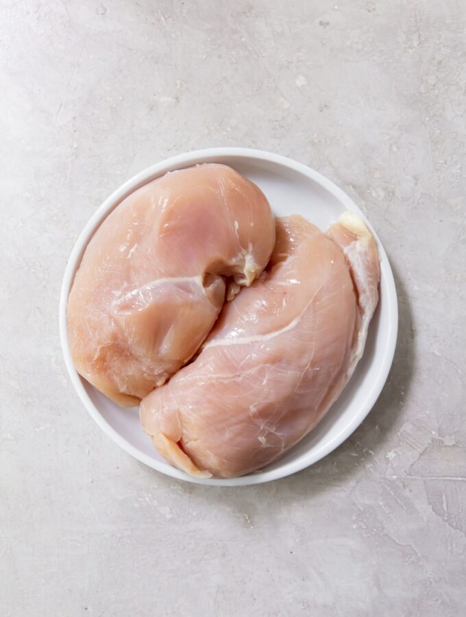 raw chicken breast on a white plate with a grey background