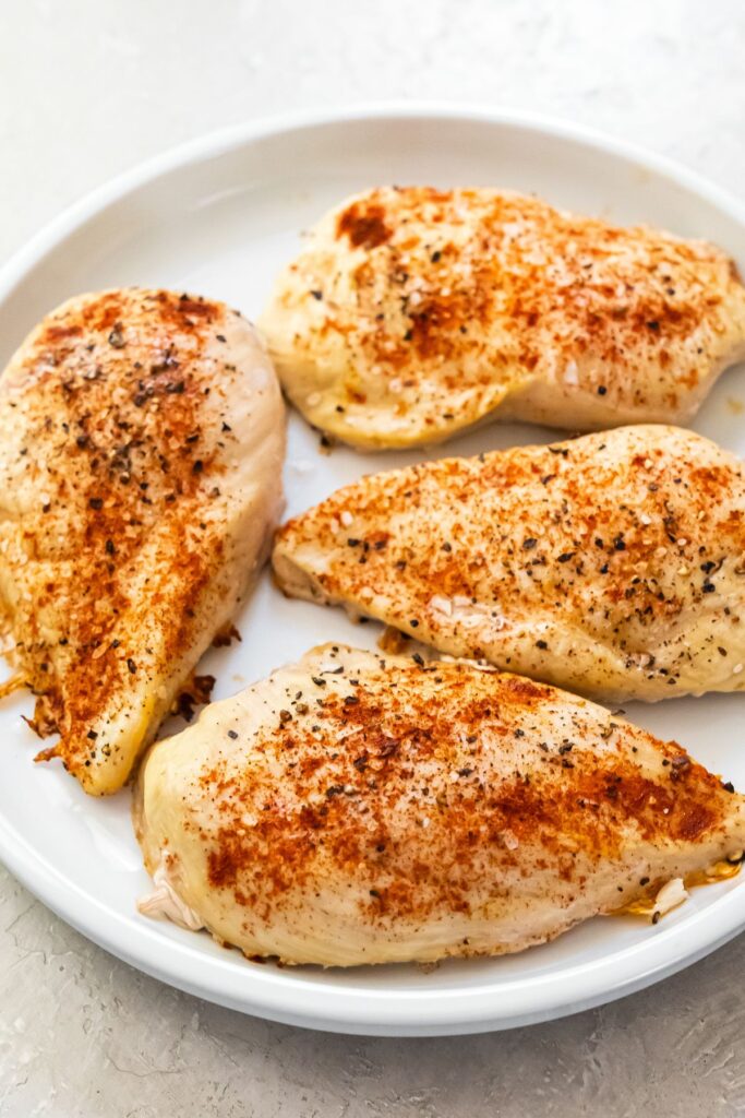 4 cooked 4 oz chicken breasts on a white plate topped