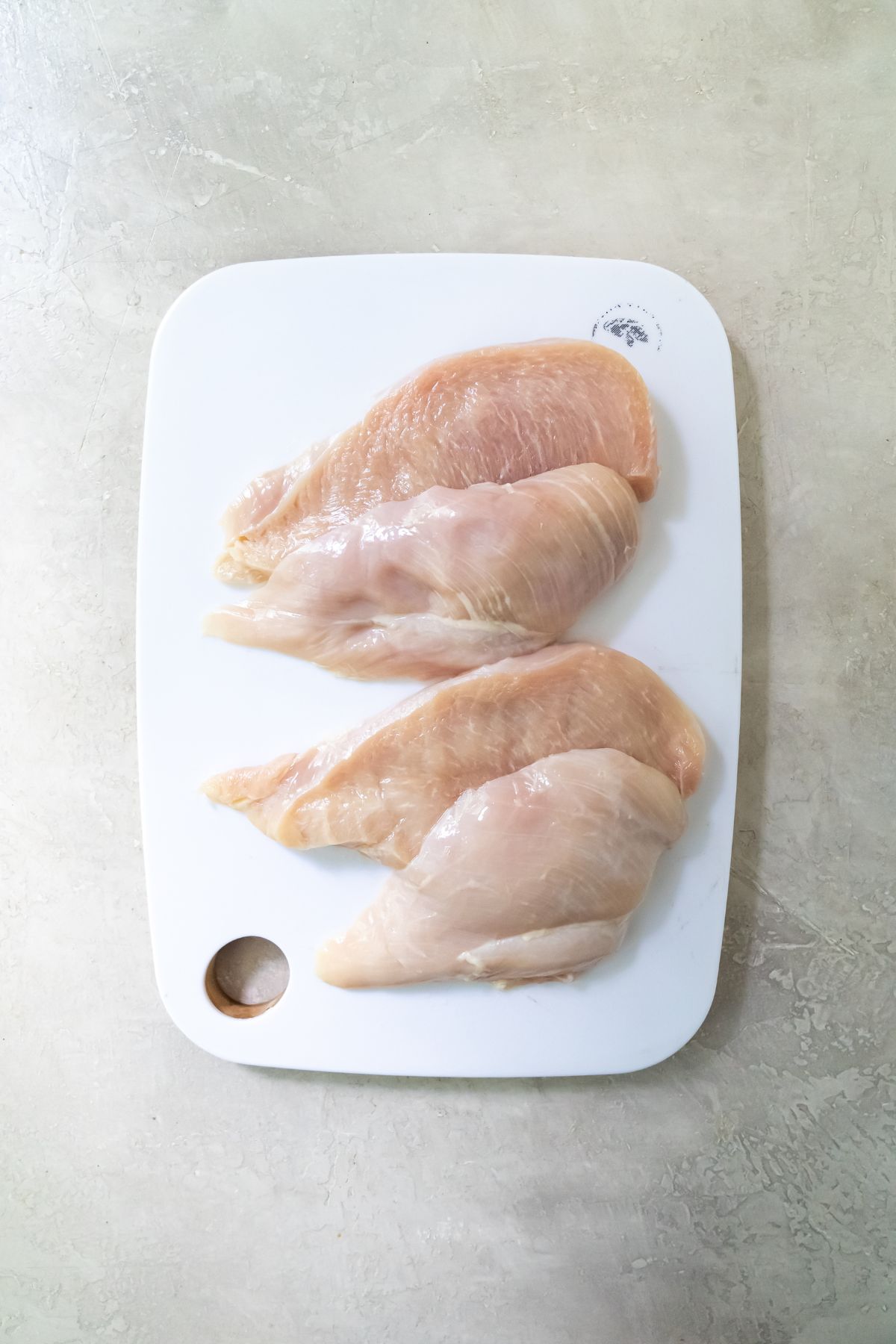 raw chicken sliced in half on a white cutting board.
