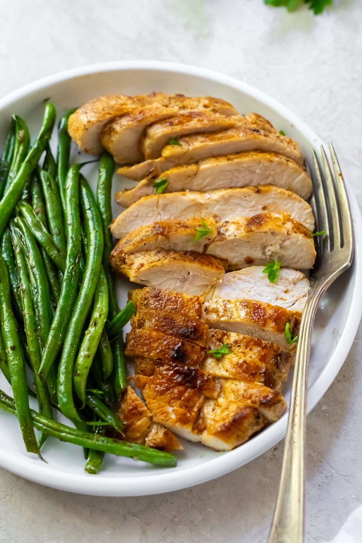 sliced chicken breast with green beans on a white plate.