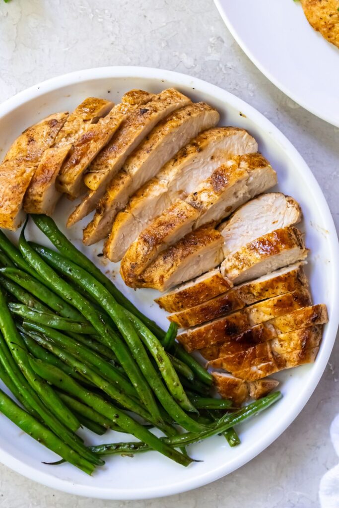 sliced chicken breast with green beans on a white plate