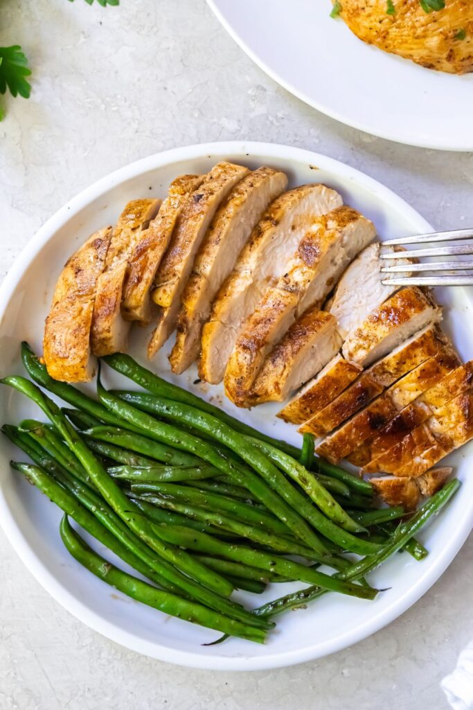 green beans on a white plate with a chicken breast and a fork with green beans