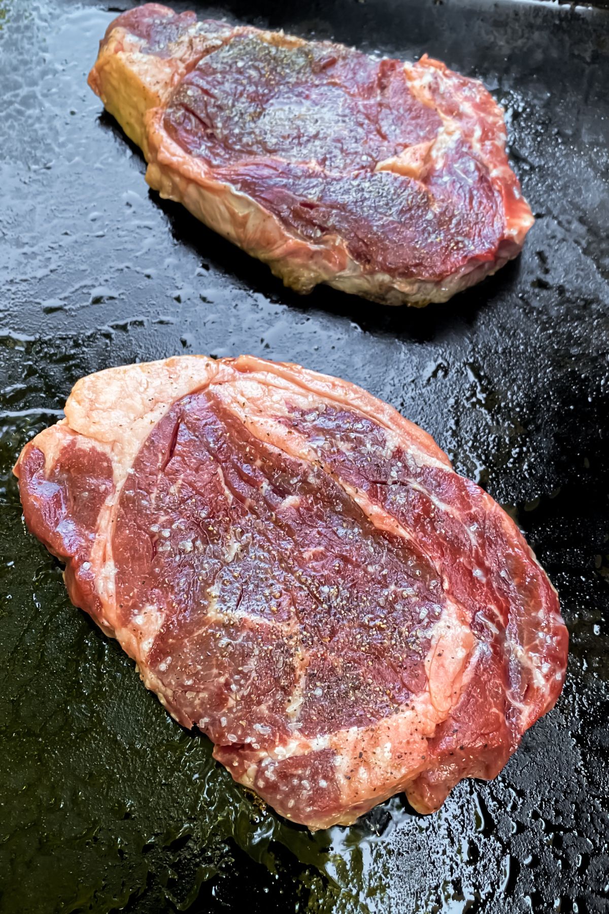 two raw ribeye steaks on a Blackstone Griddle.