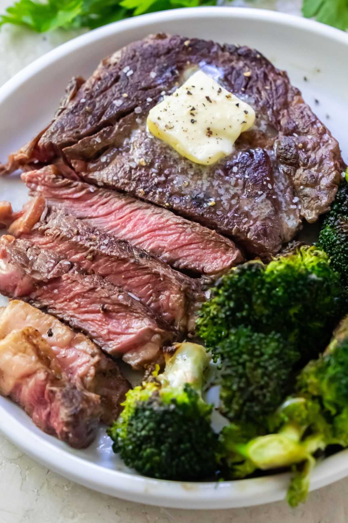 a medium rare ribeye steak that has been sliced on a white plate with a side of broccoli topped with butter.