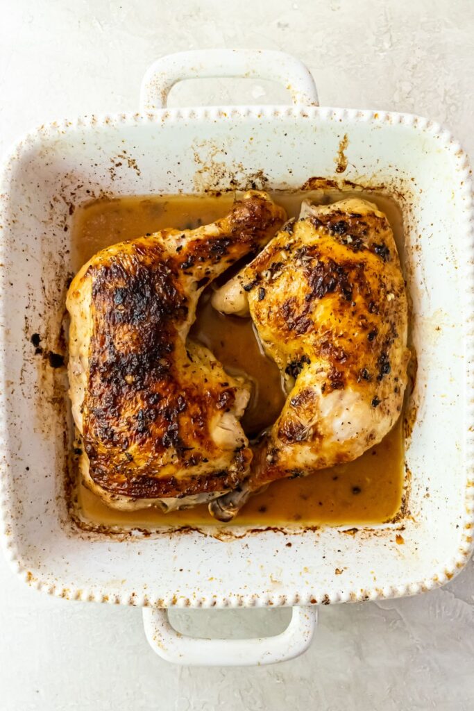 broiled chicken quarters in a white baking dish