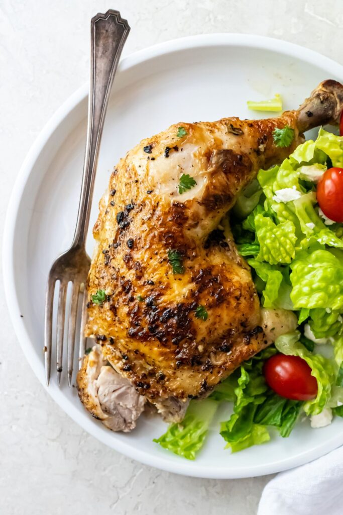 broiled chicken leg quarters on a white plate with a salad and a fork