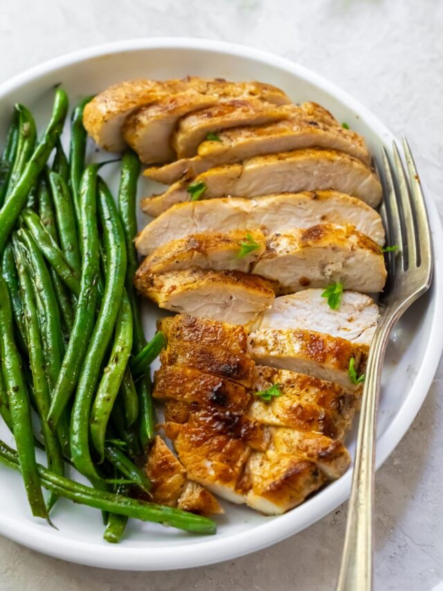 sliced chicken breast with green beans on a white plate.