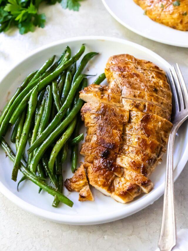 cooked and sliced chicken breast on a white plate with green beans