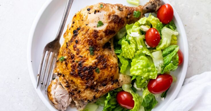 broiled chicken leg quarters on a white plate with a salad and a fork