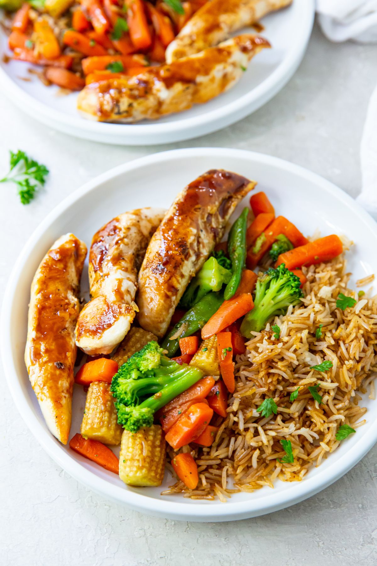 teriyaki chicken tenders, fried rice and teriyaki vegetables on a white plate