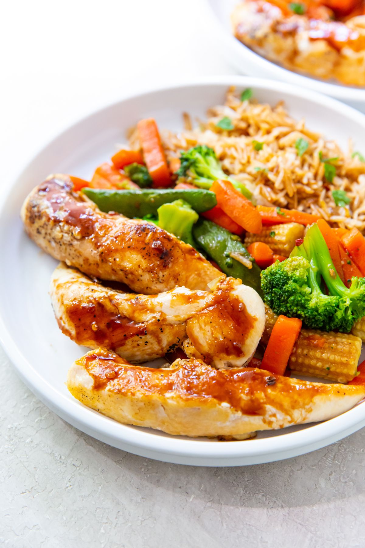 teriyaki chicken tenders made on the blackstone, fried rice and teriyaki vegetables on a white plate