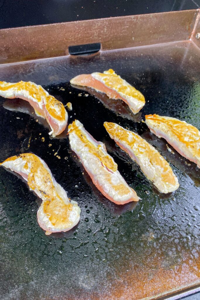 chicken tenders cooking on a blackstone griddle