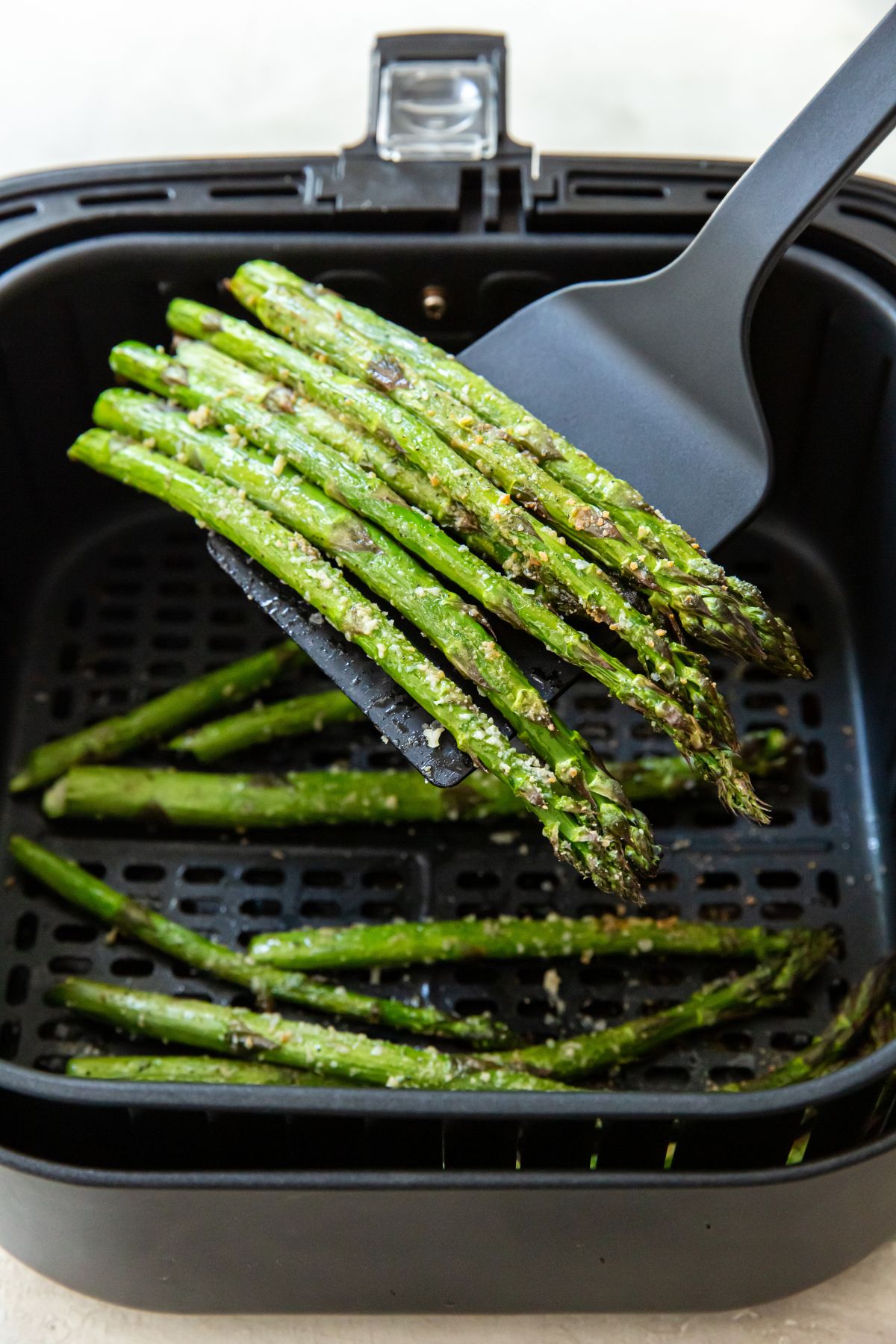 cooked asparagus in the air fryer being lifted by a spatula