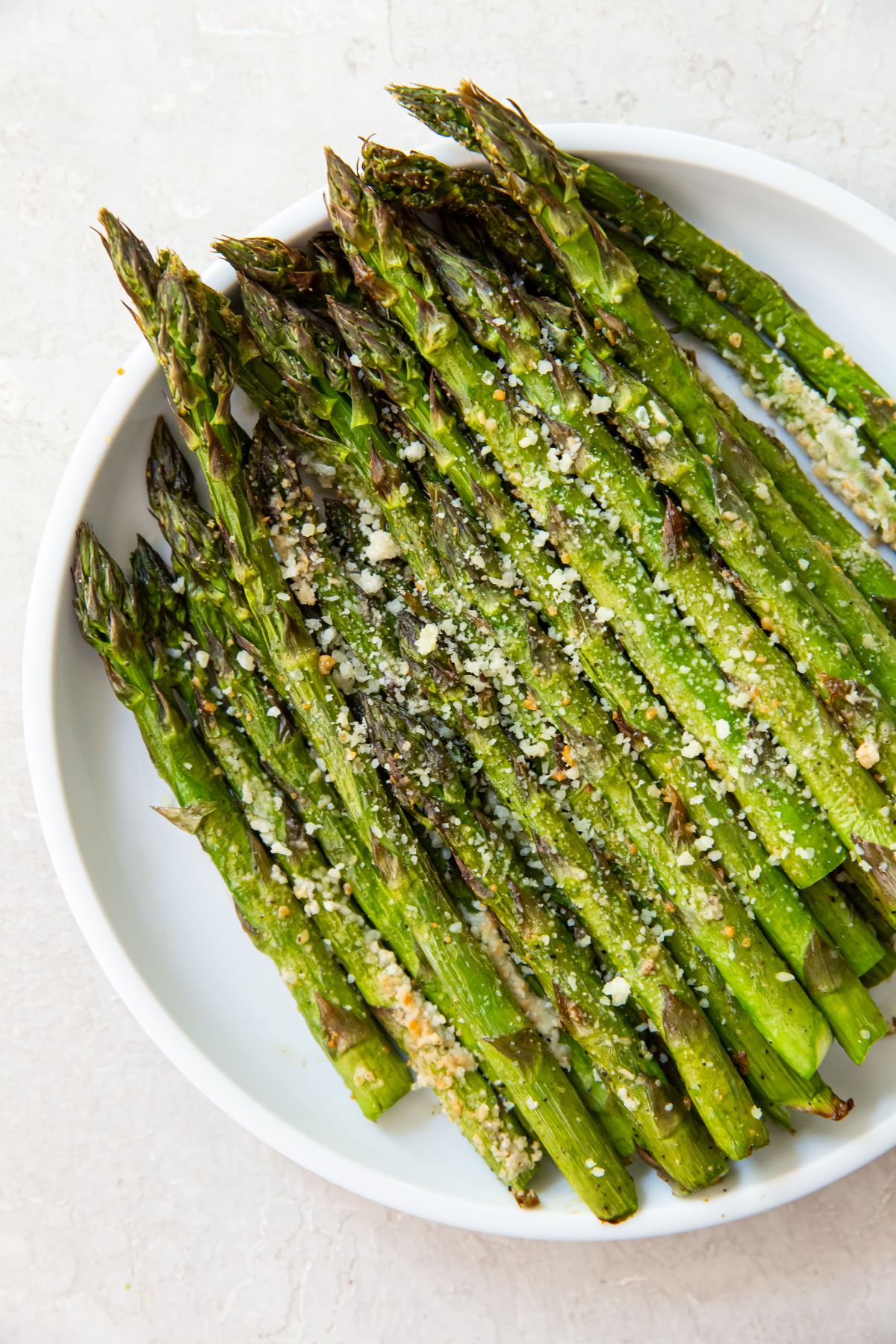 cooked asparagus on a white plate topped with Parmesan Cheese 
