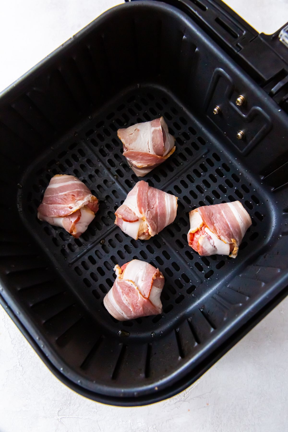 raw meatballs with bacon wrapped around them in the air fryer