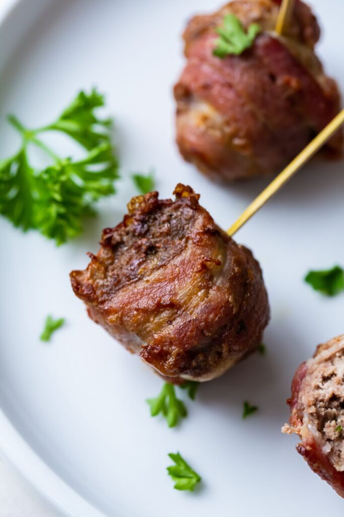 cooked bacon wrapped meatballs on a white plate with a toothpick in it