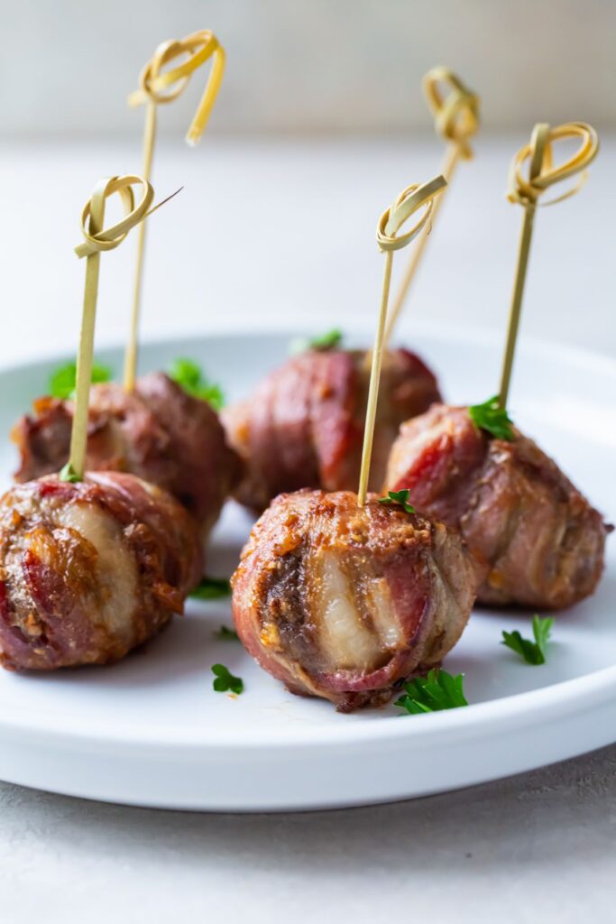 cooked bacon wrapped meatballs on a white plate with a toothpick in them on a white plate
