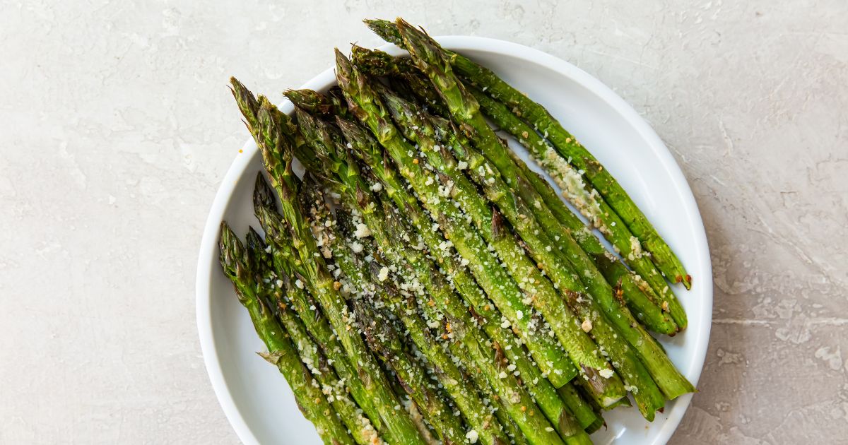 cooked asparagus on a white plate topped with Parmesan Cheese
