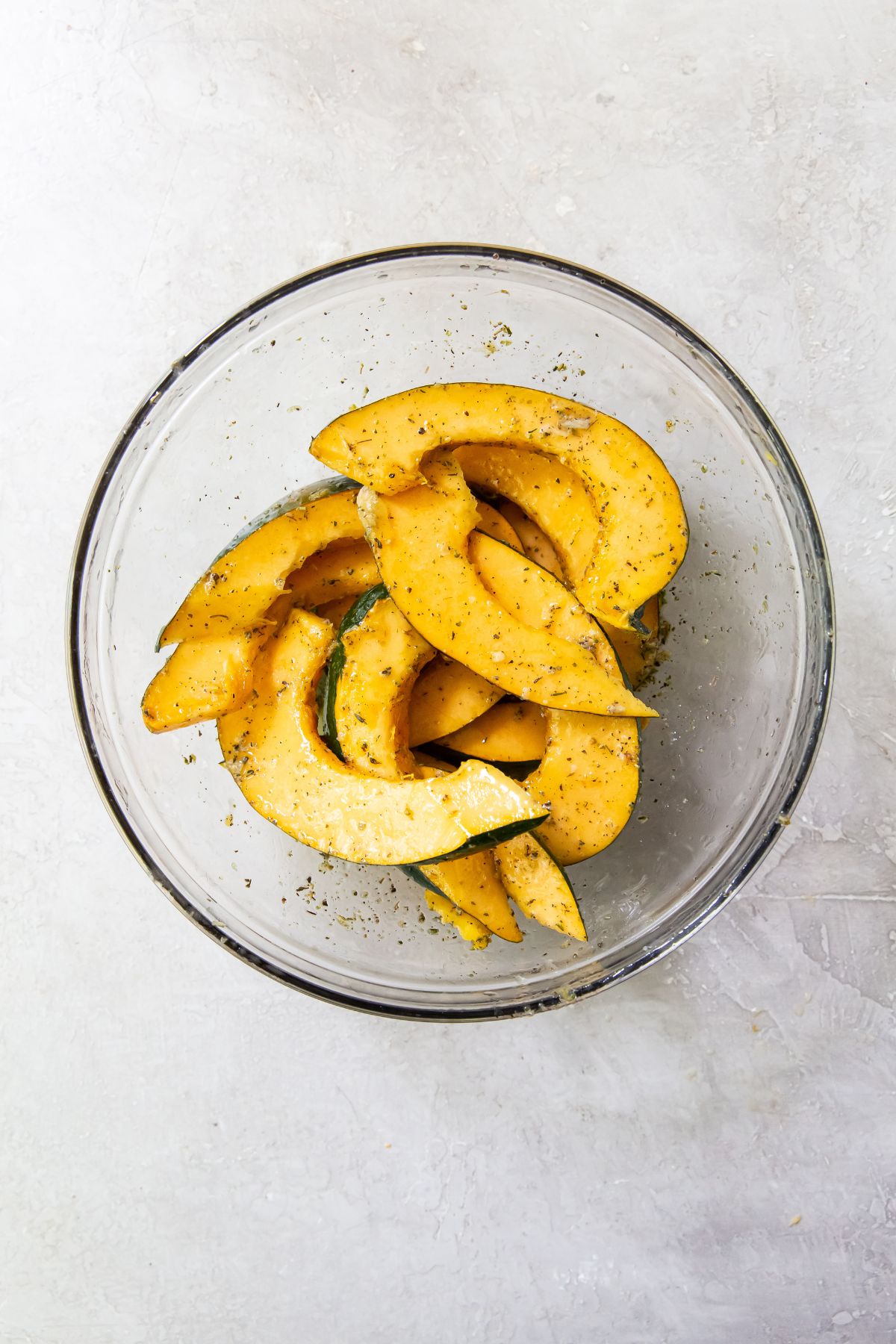 Acorn squash coated in oil and spices in a glass bowl on a white tabletop