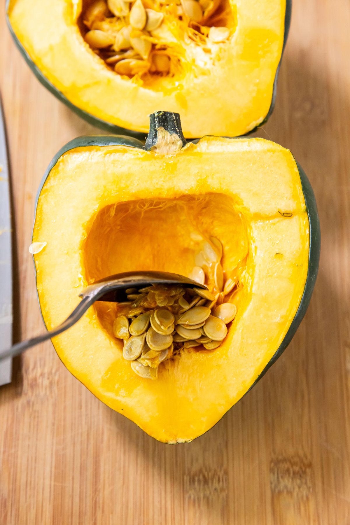 Halved acorn squash with a spoon scooping out seeds on a wooden cutting board