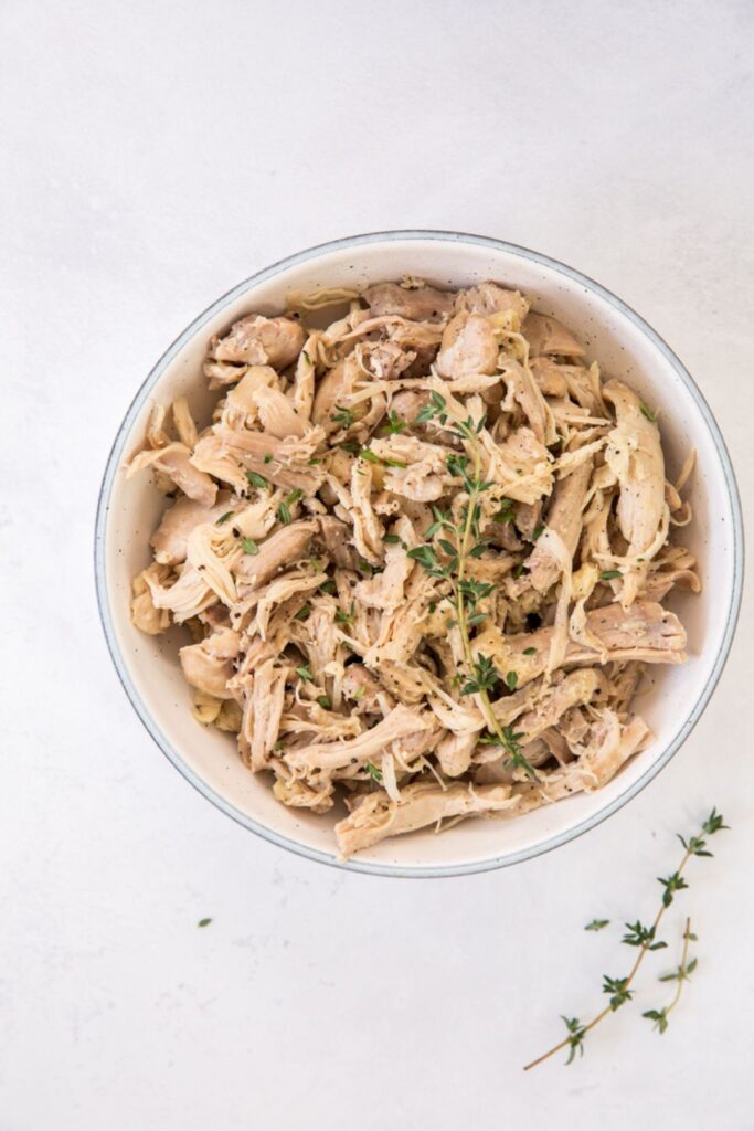 shredded chicken thighs in a white bowl with green garnish