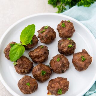 Cooked meatballs with a basil garnish on a while plate