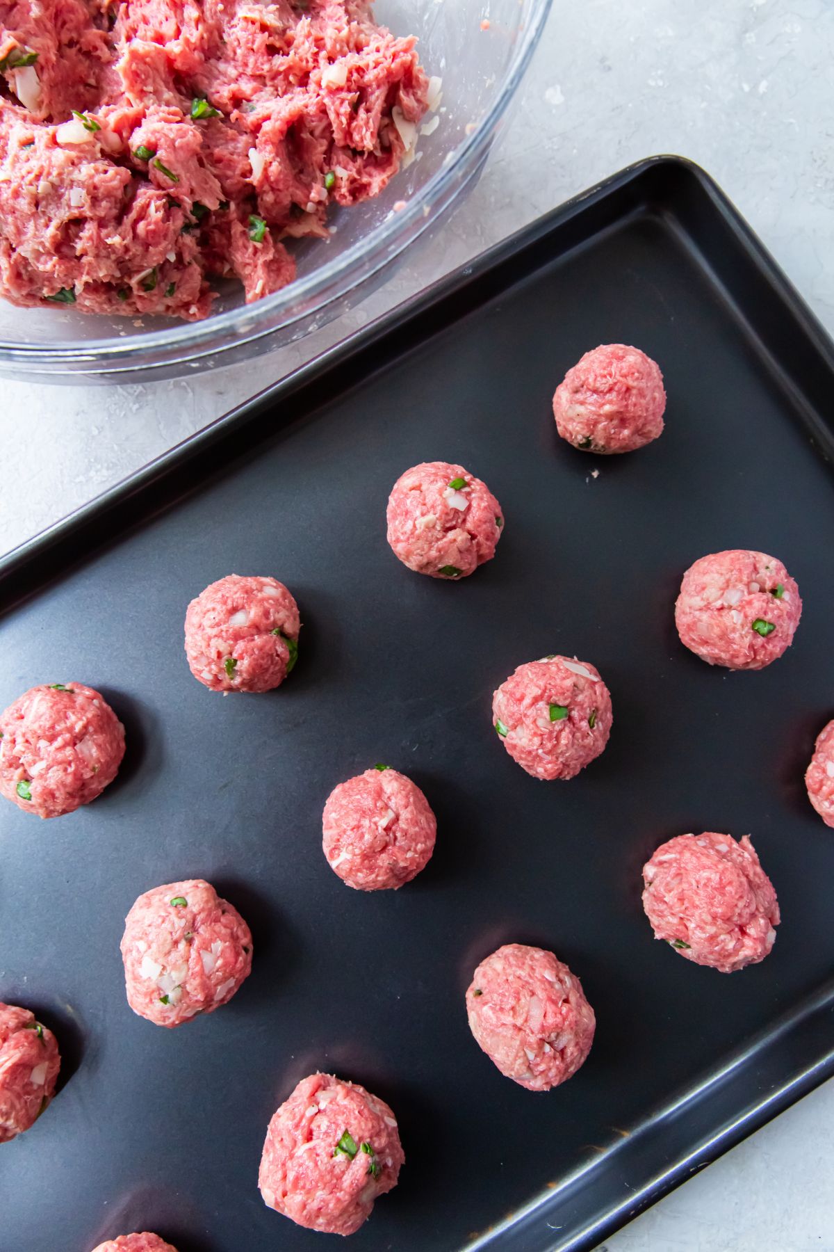 two inch meatballs neatly organized in rows of four on a black baking sheet.
