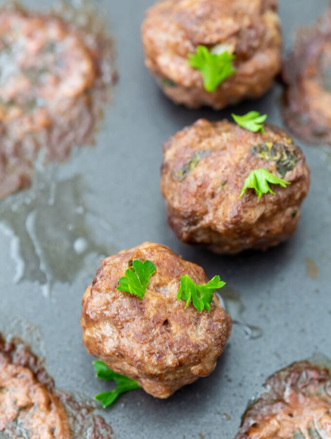 cooked meatballs topped with chopped parsley on a black baking sheet.